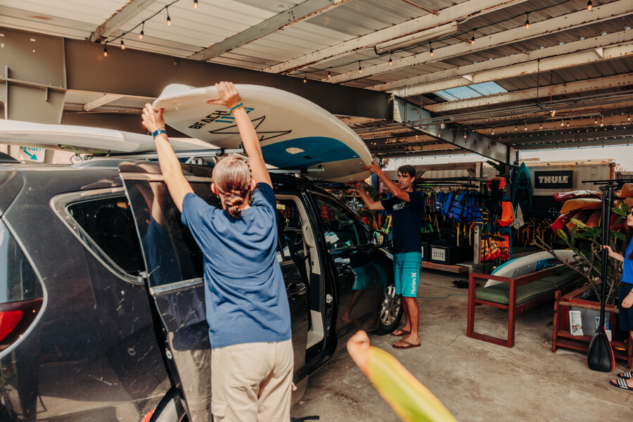 Active Oahu staff lift a paddle board on top of a vehicle