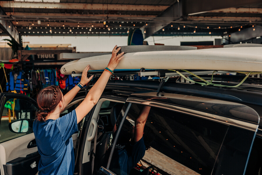 Active Oahu staff member places small foam pads on top of a paddleboard sitting on top of a vehicle