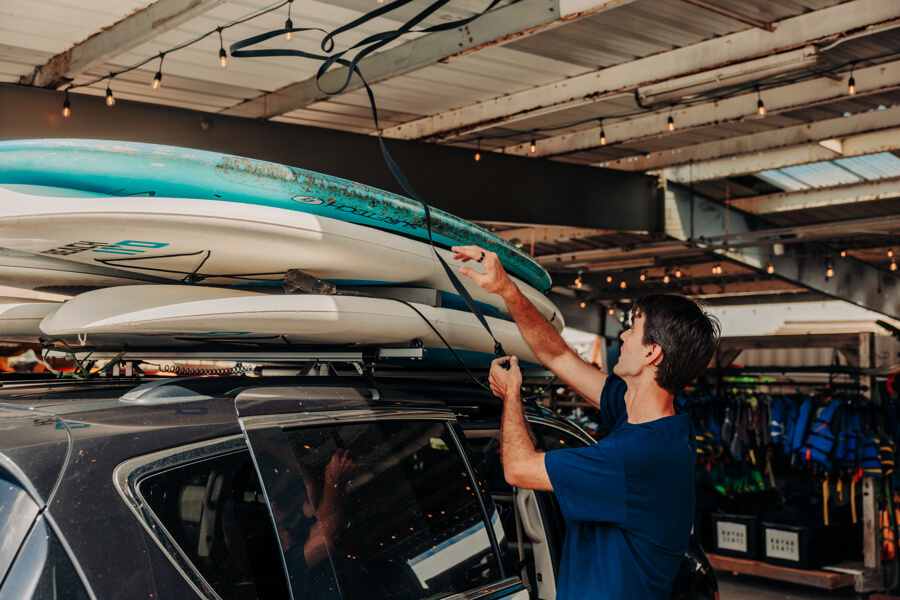 Active Oahu staff throw a strap over paddleboards on a vehicle