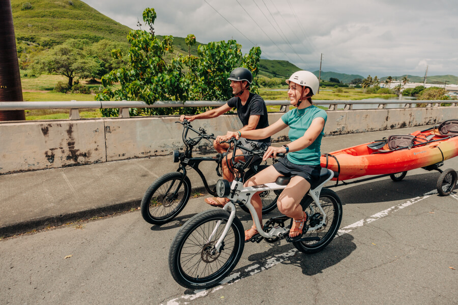 a man tows a kayak with an e-bike equipped with a trailer and a girl rides an e-bike