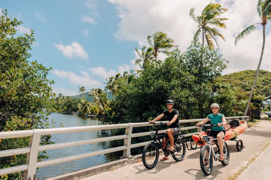 two people towing a tandem kayak rental from Active Oahu with an e-bike equipped with a kayak trailer.