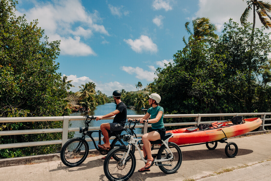 Two people e-bike across a bridge with their kayak rental from Active Oahu