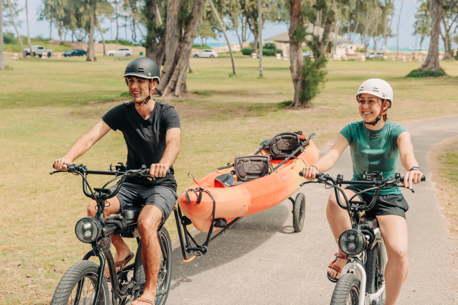 Two people on electric bike rentals from Active Oahu on a path toward the beach.