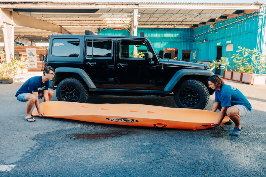 Active Oahu staff crouch to begin lifting a kayak