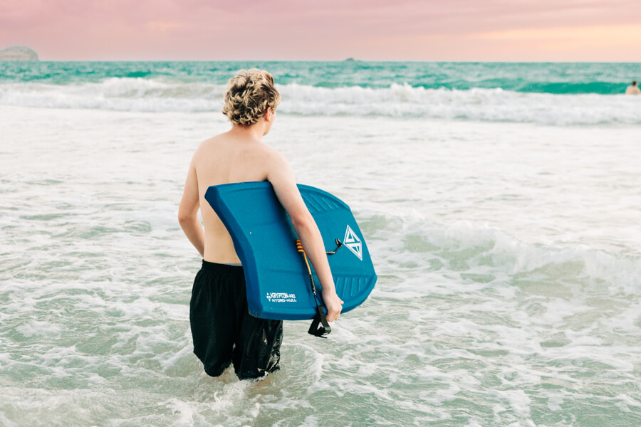 A boy holds a boogie board rental from Active Oahu while walking into the waves.