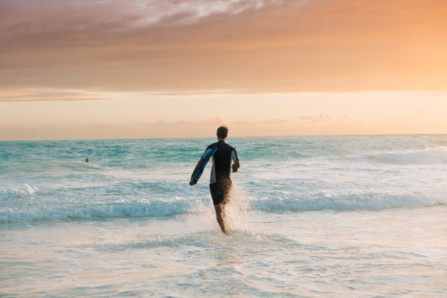A person runs into a wave holding a boogie board rental from Active Oahu