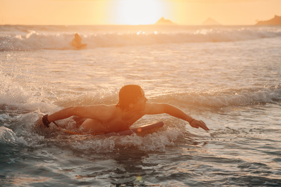 A boy catches a wave on his boogie board rental from Active Oahu at sunset