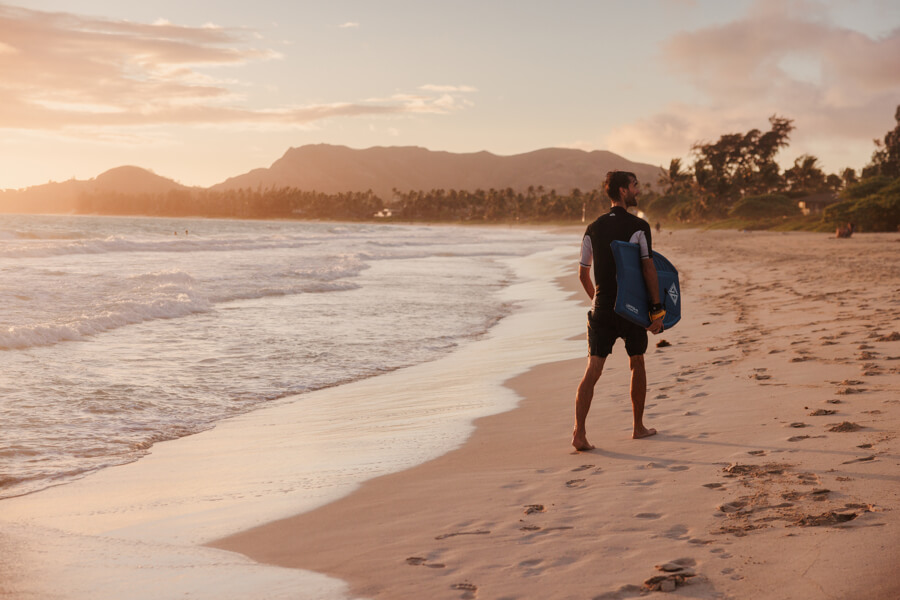 A man carries his boogie board rental from Active Oahu while walking on Kalama Beach