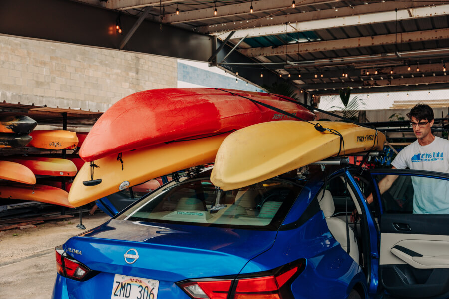 Three kayak rentals from Active Oahu are strapped on top of a sedan.