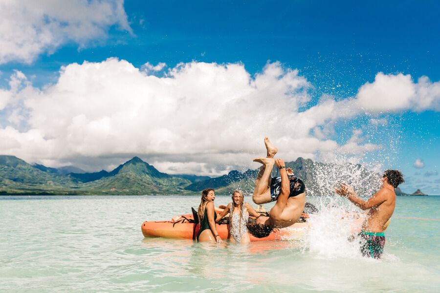 A group of young adults playing in the water at the Kaneohe Sandbar in front of their kayak rental from Active Oahu