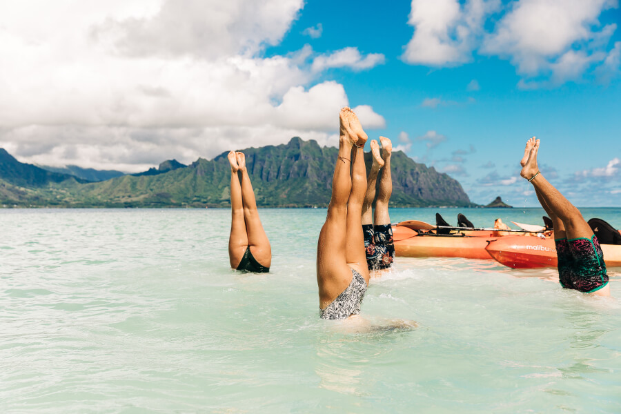 A group of young adults doing handstands under the water next to their kayak from Active Oahu